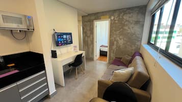 Una habitación con kitchenette, escritorio con computadora, sofá y ventana con vista a edificios.