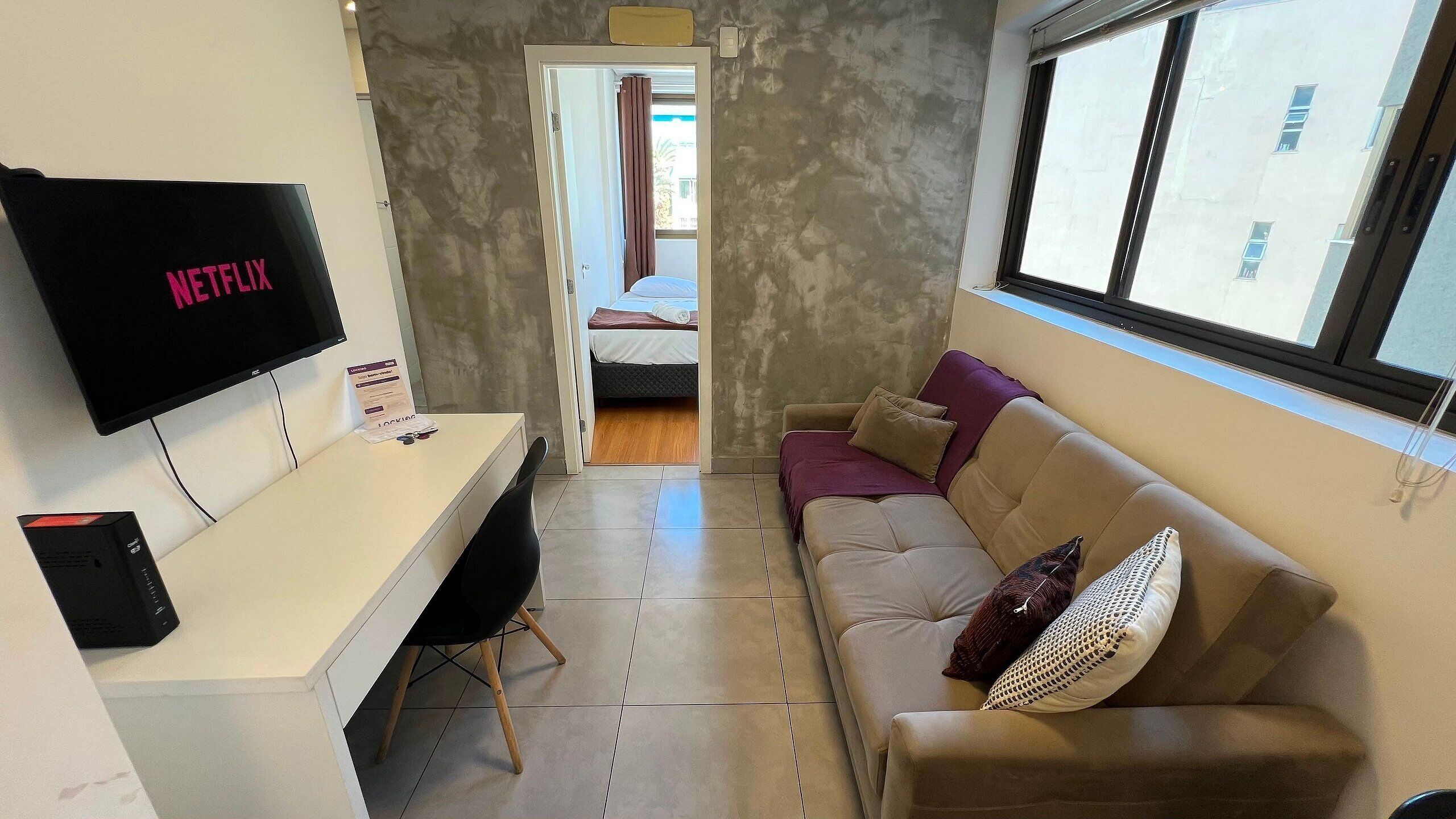 Habitación de hotel pequeña con cama, escritorio con computadora, televisor y sofá.