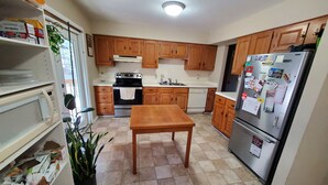 Una cocina con armarios de madera, un refrigerador de acero inoxidable, una mesa de madera y piso de baldosas.