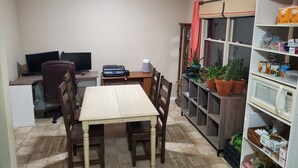 Un comedor con mesa y sillas, un escritorio con monitor e impresora, y una estantería con diversos objetos.