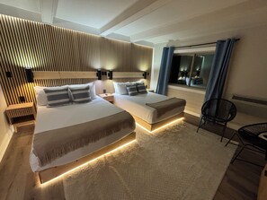 Un dormitorio moderno con una cama grande, mesitas de noche, un pequeño sofá, una silla y un ventanal con cortinas.
