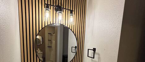 A bathroom with a white sink, a round mirror, and vertical wooden paneling.