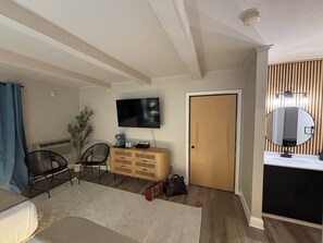 Una habitación con una cama, un televisor en la pared, un armario de madera, un espejo y una puerta.