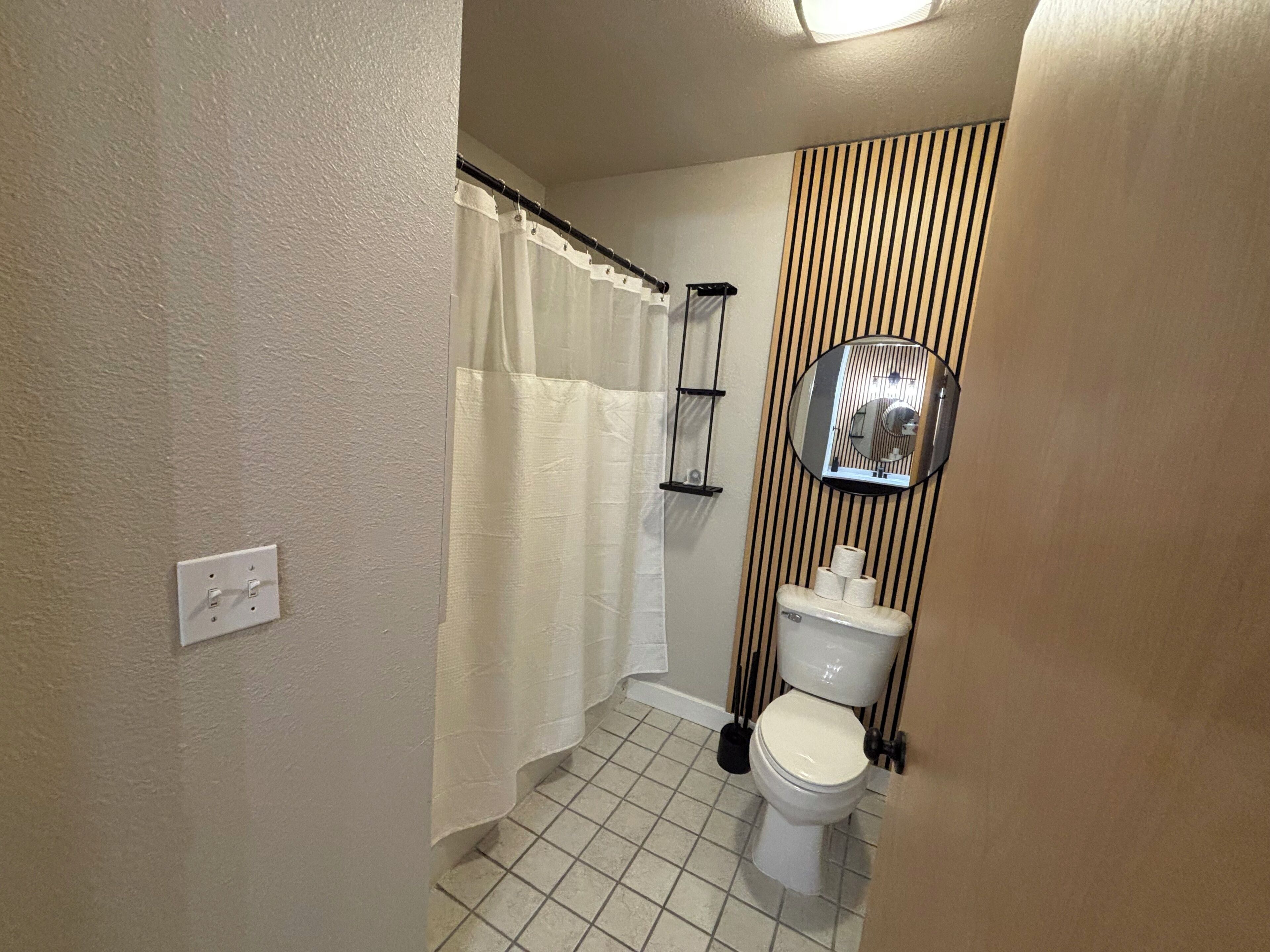 A bathroom with a toilet, a shower curtain, a mirror, and a toilet paper holder.
