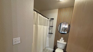 A bathroom with a toilet, a shower curtain, a mirror, and a toilet paper holder. - King Room Near Torch Lake | Hot Tub, Sauna, Resort Amenities (Rapid City)