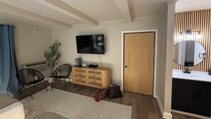 A room with a bed, a TV mounted on the wall, a wooden cabinet, a mirror, and a door. - King Room Near Torch Lake | Hot Tub, Sauna, Resort Amenities (Rapid City)