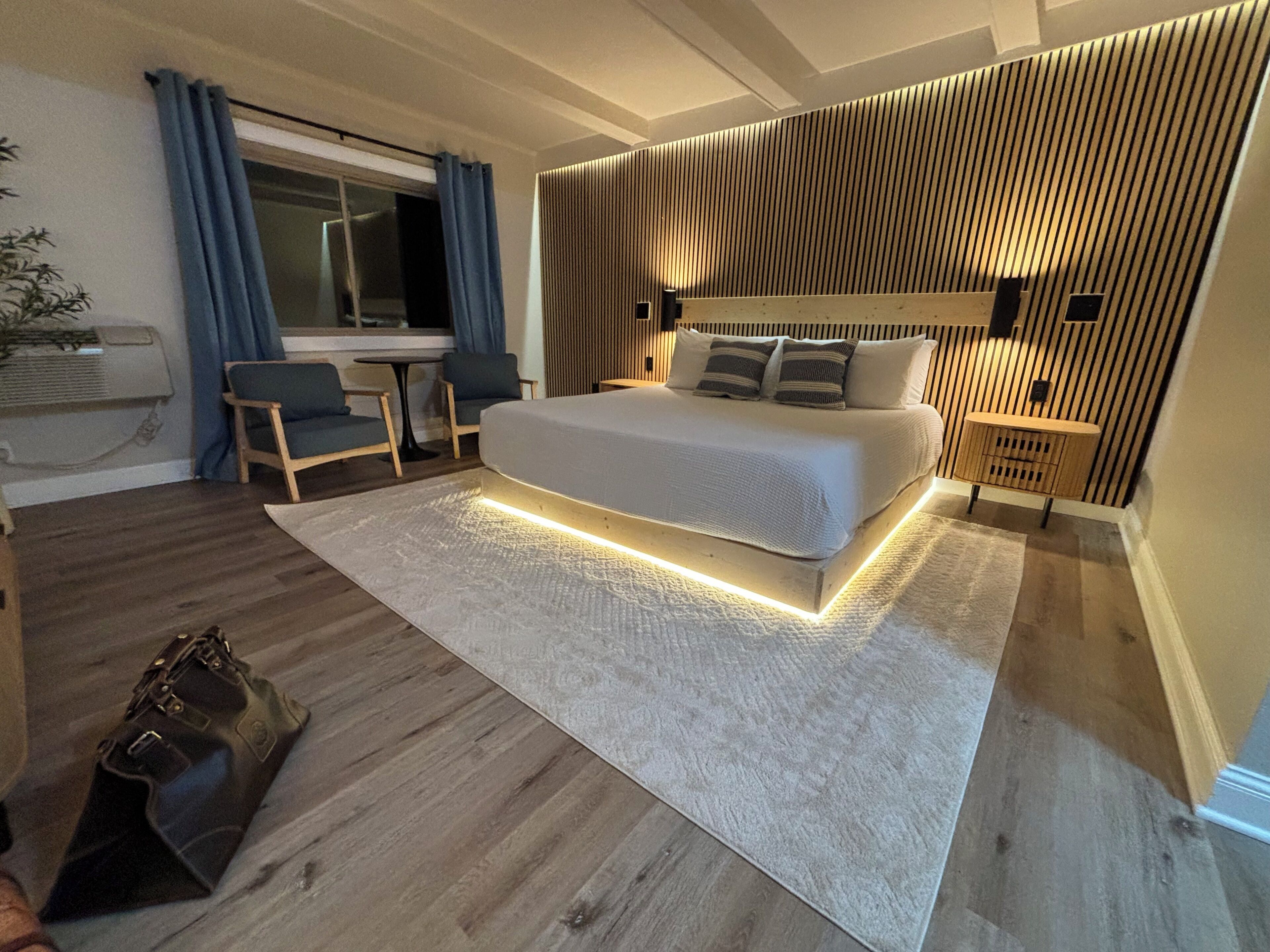 Ein modernes Schlafzimmer mit einem großen Bett, einem Schreibtisch, einem Sessel, einem kleinen Tisch und einer Wandlampe.
