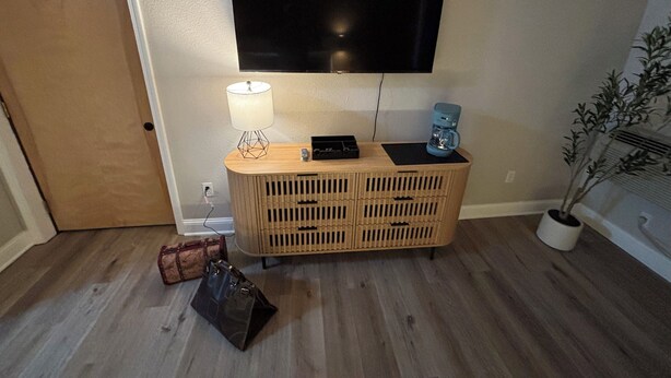 A room with a wooden cabinet, a flat-screen TV mounted on the wall, a lamp on the cabinet, a coffee maker, a suitcase, and a potted plant. - King Room Near Torch Lake | Hot Tub, Sauna, Resort Amenities (Rapid City)