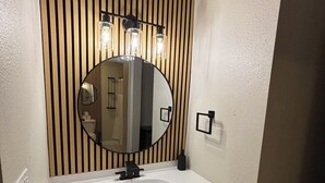 Une salle de bain avec un lavabo blanc, un miroir rond et un lambris en bois vertical.