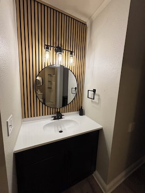 Un baño con un lavabo blanco, un espejo redondo y paneles de madera verticales.