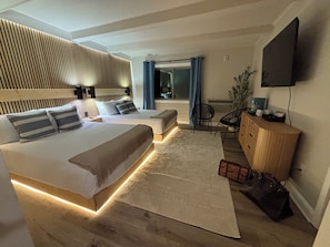Una habitación de hotel moderna con una cama grande, mesitas de noche, un escritorio, una silla, un televisor y una planta.