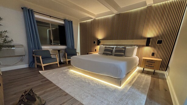 Une chambre moderne avec un grand lit, un bureau et une chaise, une petite table et une lampe fixée au mur.