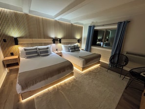 Un dormitorio moderno con una cama grande, mesitas de noche, un pequeño sofá, una silla y un ventanal con cortinas.