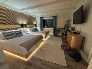 Una habitación de hotel moderna con una cama grande, mesitas de noche, un escritorio, una silla, un televisor y una planta.