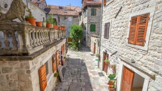 A narrow stone-paved street flanked by traditional stone buildings with wooden shutters and balconies. - Majka Guest House (Kotor)