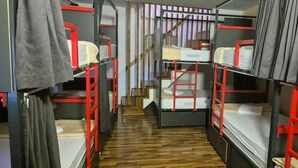 A narrow corridor with bunk beds on either side, a wooden staircase in the center, and a grey curtain on the left. - Majka Guest House (Kotor)