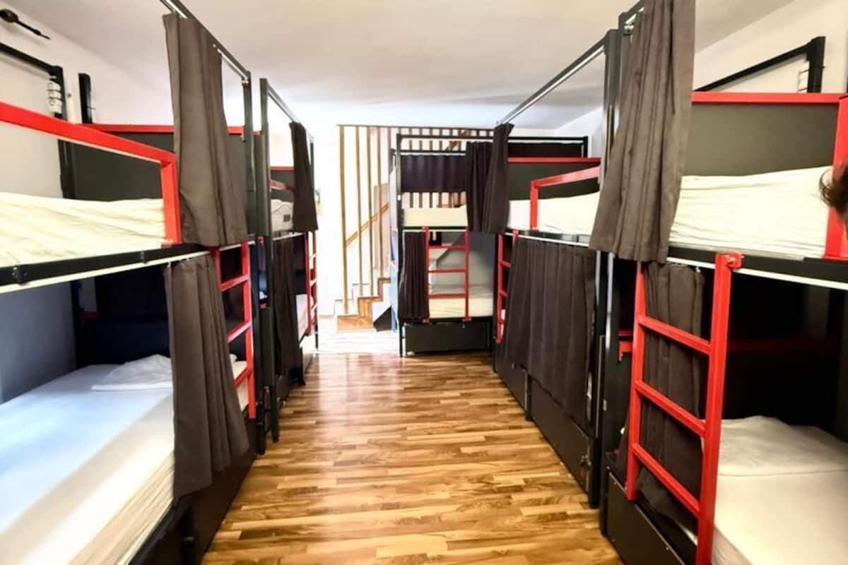 Un pasillo con literas a ambos lados, suelo de madera y una escalera en el centro.