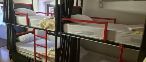 A bunk bed with red railings, a white mattress, and a beige blanket on the top bunk.