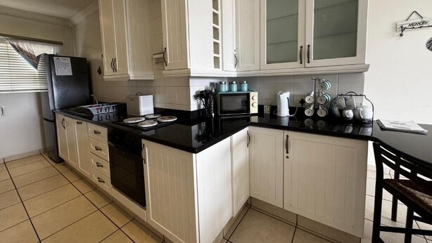 A kitchen with white cabinets, a black countertop, a refrigerator, a microwave, and a coffee maker. - Mangrove Beach Estate Boboyi (Port Shepstone)