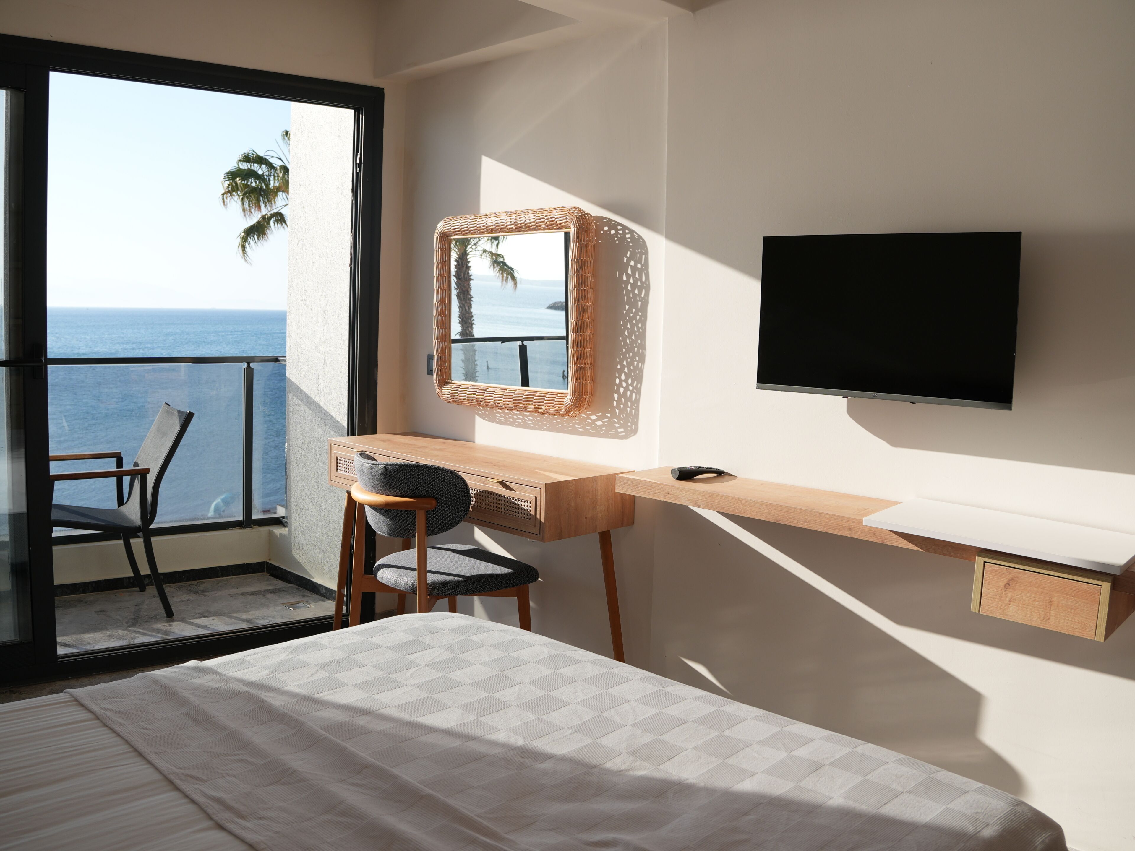 Quarto com cama, escrivaninha, cadeira, televisão e varanda vista para o mar.