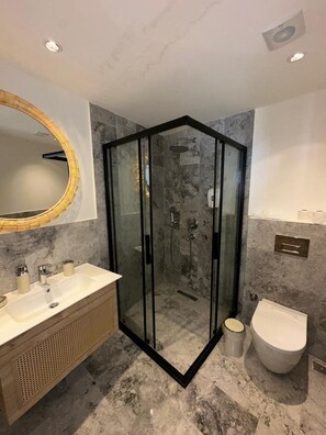 A modern bathroom with a glass-enclosed shower, a vanity with a sink, and a toilet. - ÇİFTLİQUE (Cesme)