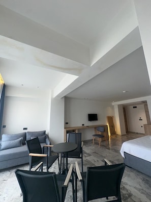 Quarto de hotel moderno com sofá, mesa de jantar, cadeiras, televisão e cama.