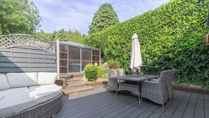 A deck with a sofa, a table with chairs, a pergola, and a hedge. - Stylish 3BR Home | Hot Tub | Near NEC, HS2 & JLR (West Midlands)