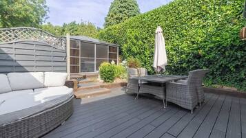 Een terras met een bank, een tafel met stoelen, een pergola en een haag.