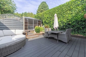 A deck with a sofa, a table with chairs, a pergola, and a hedge.