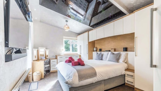 A modern bedroom with a large bed, built-in wardrobe, and a ceiling with exposed beams. - Stylish 3BR Home | Hot Tub | Near NEC, HS2 & JLR (West Midlands)