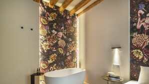 Un baño moderno con una bañera independiente, una mesita de noche redonda con lámpara y una cama con alfombra roja.