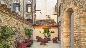 Un estrecho patio con pared de ladrillo, techo de tejas y una pequeña zona de estar con sofá y sillones.