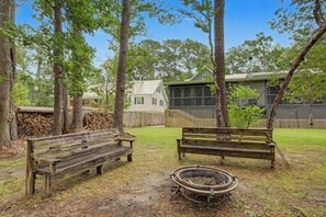 A wooden bench in a yard with a fire pit, surrounded by trees and a house in the background. - Downtown and Beach accessible Hot Tub + Firepit (Mobile)