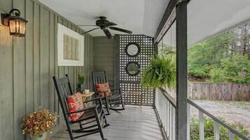 A covered porch with a ceiling fan, outdoor seating with chairs and cushions, and a decorative wall with circular cutouts.