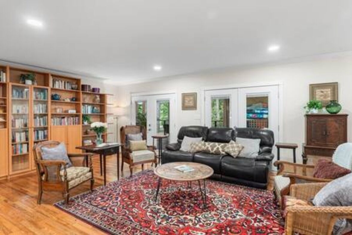 A living room with a black leather sofa, a patterned rug, and a bookshelf filled with books.
