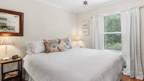 Un dormitorio con cama, mesitas de noche, ventilador de techo y ventana con cortinas.