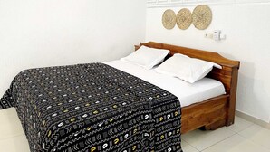 A bedroom with a wooden bed, white bedding, a patterned bedspread, and decorative wall hangings.
