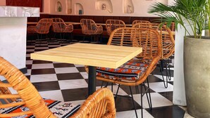 A restaurant interior with checkered flooring, wicker furniture, and a wall with built-in shelves displaying various items.