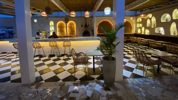 A restaurant with checkered flooring, a bar area, and wicker chairs.