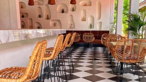 A checkered floor, wicker chairs, a bar area, and a wall with shelves.