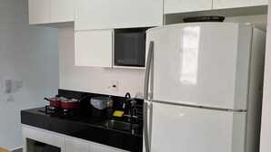 Uma cozinha moderna com armários brancos, uma geladeira Bosch, bancada preta e micro-ondas sobre o fogão.