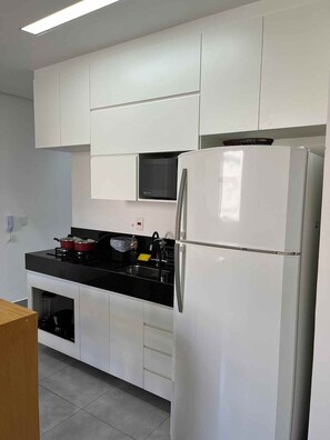 Une cuisine moderne avec des meubles blancs, un réfrigérateur Bosch, un plan de travail noir et un four à micro-ondes placé au-dessus de la cuisinière.