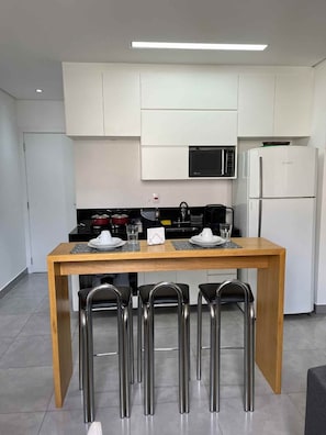 Une cuisine moderne avec des meubles blancs, un réfrigérateur Bosch, un four à micro-ondes et une table à manger avec quatre chaises.