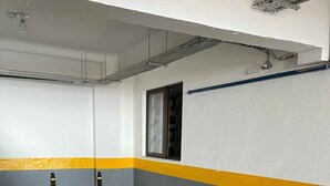 Um estacionamento com piso de concreto, paredes pintadas de amarelo e cinza, e uma janela com moldura de metal.
