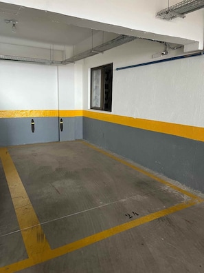 Un parking avec un sol en béton, des murs peints en jaune et en gris, et une fenêtre dotée d’un cadre en métal.