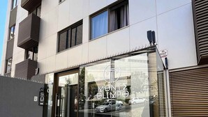 Un edificio moderno con fachada de vidrio, un logotipo visible y una pequeña jardinera con césped.