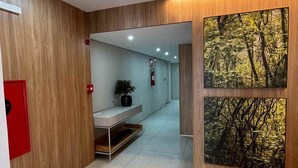 Un pasillo moderno con paneles de madera, un extintor, una planta en maceta y una fotografía en grande de un bosque enmarcados.
