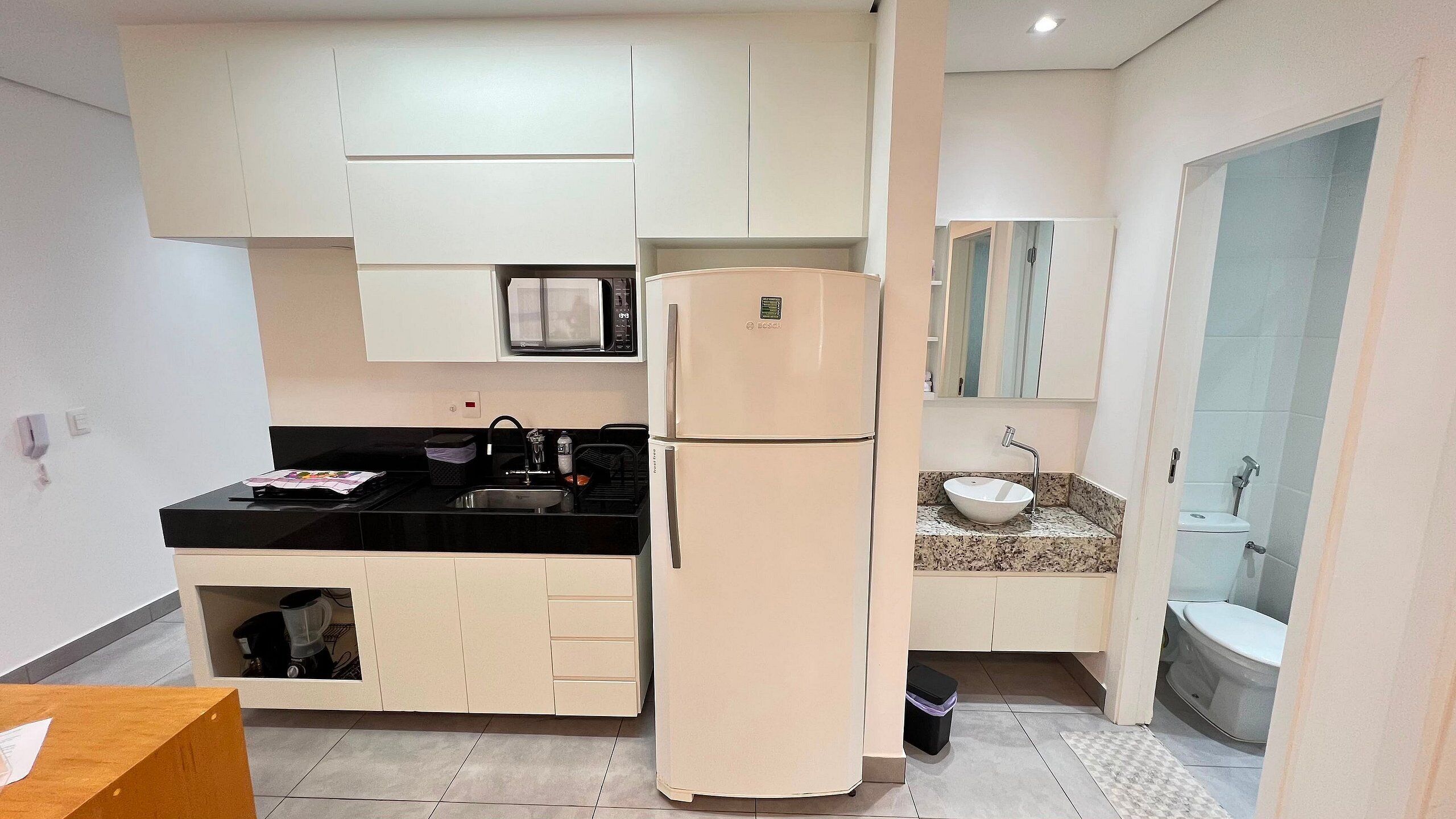 Una cocina compacta con refrigerador, microondas y lavamanos con encimera de granito.