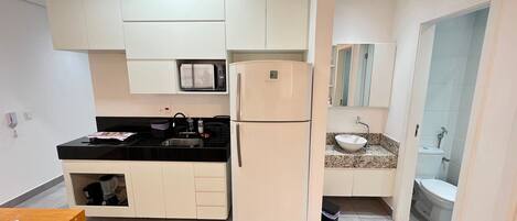 Una cocina compacta con refrigerador, microondas y lavamanos con encimera de granito.