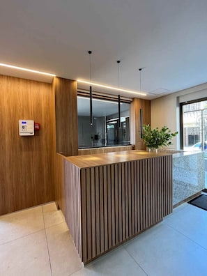 Un mostrador de recepción con detalles de madera, una lámpara colgante moderna y una planta en maceta.